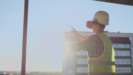 Engineer-Builder-on-the-roof-of-the-building-at-sunset-stands-in-VR-glasses-and-moves-his-hands-using-the-interface-of-the-future.-Futuristic-engineer-of-the-future.-The-view-from-the-back